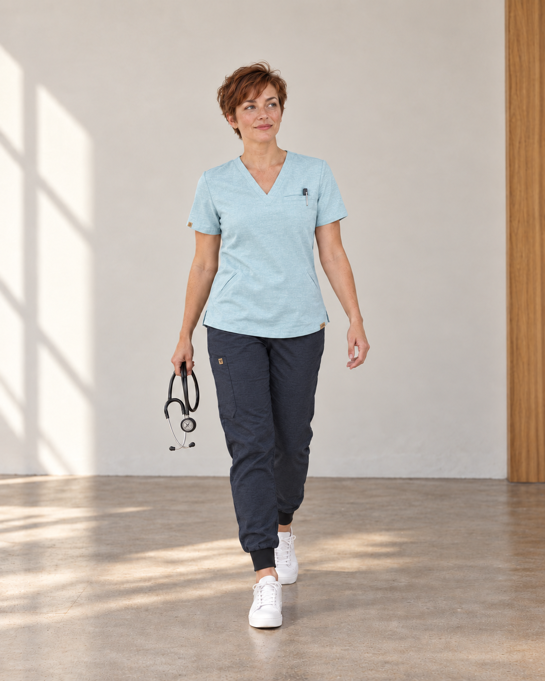 Woman wearing a light blue Siena scrub top and navy Sambe scrub pants in natural daylight
